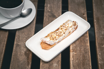 Cup of coffee and eclair on a wooden table close-up.