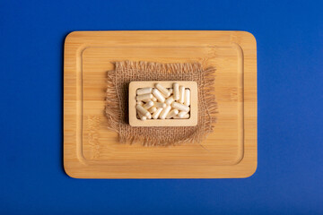 White vitamin capsules in wooden small box on a wooden desk from above in rustic style on blue background. 