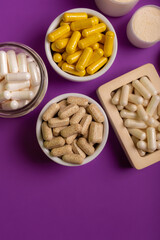 Vitamins and minerals in different forms such as capsules, tablets, pills, powder in jars on violet...