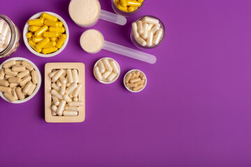 Vitamins and minerals in different forms such as capsules, tablets, pills, powder in jars on violet...
