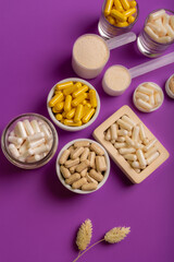 Different vitamins and minerals in form of tablets and pills in jars from above on a violet background. 