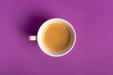 Minimalist food composition with morning aromatic americano coffee with foam on violet purple background from above. 