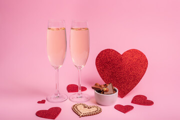 Romantic card with two glasses of champagne, milk chocolate with nuts on round white plate and red hearts on light pink background. Happy Valentine's Day.