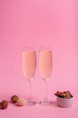 Two glasses of white sparkling wine and tasty milk chocolate with nuts in a small white plate on pink background. Beautiful holiday card.