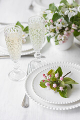 Beautiful table decor for a wedding dinner with a spring blooming apple tree flowers. Celebration of a special event. Fancy white plates, wineglasses
