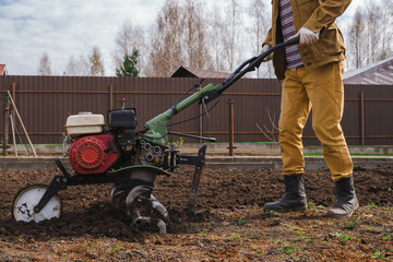 Farmer cultivates the ground soil in the garden using a motor cultivator or tiller tractor. Modern...