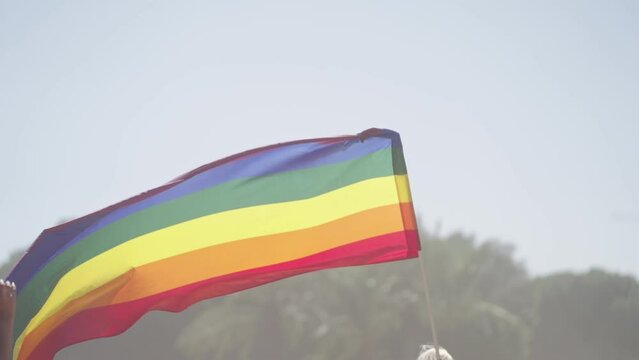 LGBTQ rainbow flag waving in slow motion during the main party in a pride parade with thousands of people