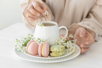 Traditional delicious French dessert - sweet homemade macarons on a vintage plate. Colourful tasty macaroons served on a white china with herbal tea. Decorated with fragile cherry tree flowers.