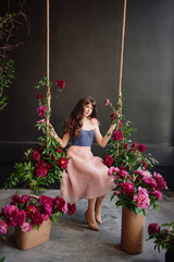 a beautiful young woman in a dress sits on a swing in peony flowers. 
