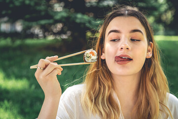 A young woman eating sushi in nature, maki roll close-up.
