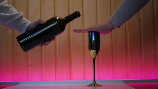 Caucasian male hand covering a wine glass and refusing to drink in beautiful atmosphere with pink backlight. Young guy refuses alcohol and won't let to fill his glass. Declining alcohol offer
