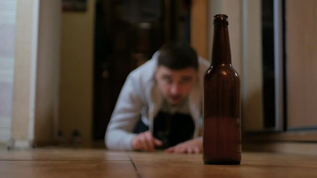 A drunken man crawling on all fours on the floor to a bottle of beer. Close-up of a glass bottle of beer and a creeping alcoholic in the background. Alcoholism concept. Alcohol abuse. Addicted person
