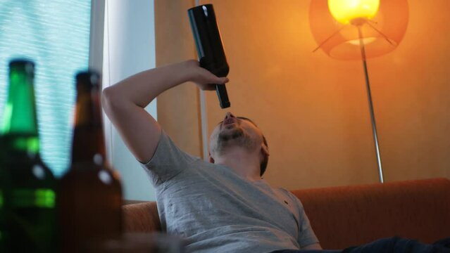 Drunk caucasian guy finishing a bottle of alcohol at home and throwing it around. Alcoholism concept. Inadequate addicted alcoholic realizing that booze ran out throwing the bottle in frustration