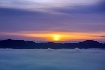 Foggy clouds fell below mountain level at sunrise, orange horizon, violet