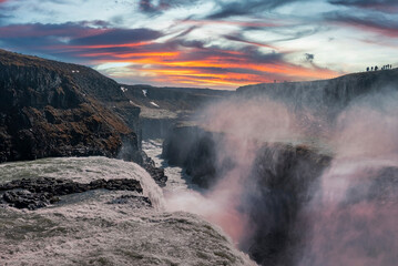 Beautiful view of Gullfoss waterfall in Golden Circle. Idyllic view of falling water against cloudy sky. Picturesque scenery of cascades amidst rock formations in valley during sunset.