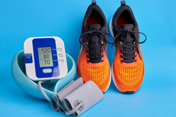 Orange sneakers and blood pressure monitor in a heart-shaped bowl on a blue background