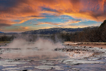 Smoke emitting from geothermal field in Smidur Geyser. Beautiful landscape view of valley against cloudy sky. Dramatic land of tourist attraction during sunset.