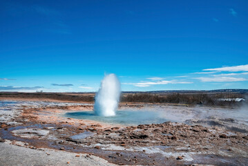 Beautiful eruption of Strokkur geyser amidst landscape. Powerful smoke emitting from land against...