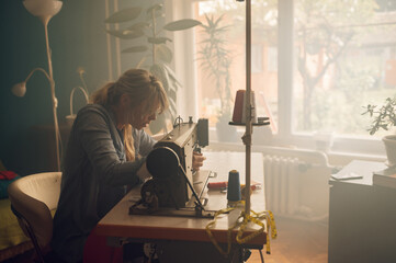 Tailor woman sitting and sewing on a sewing machine a in studio