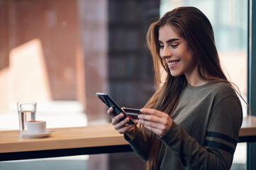 Woman using smartphone and a credit card for online shopping in a cafe