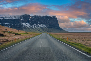 Naklejka premium Diminishing highway leading towards mountain. Empty road against cloudy sky during sunset. Scenic view of street amidst volcanic landscape during stormy weather.
