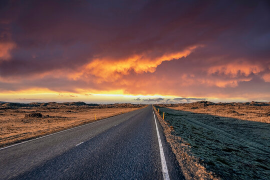 Empty highway amidst volcanic landscape. Diminishing road against dramatic sky during sunset. Scenic view of street in northern Alpine region during stormy weather.
