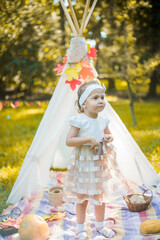 Little girl lying and playing in a tent, children's house wigwam in park Autumn portrait of cute curly girl. Harvest or Thanksgiving. autumn decor, party, picnic. Child in white dress with pumpkins.  © MartaKlos