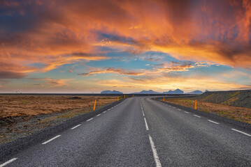 Fototapeta na wymiar Diminishing empty road amidst volcanic landscape. Road markings on street on mountain against cloudy sky. Scenic view of highway with yellow poles on roadside during sunset.
