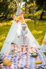 Little girl lying and playing in a tent, children's house wigwam in park Autumn portrait of cute curly girl. Harvest or Thanksgiving. autumn decor, party, picnic. Child in white dress with pumpkins.  © MartaKlos