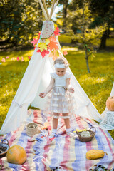 Little girl lying and playing in a tent, children's house wigwam in park Autumn portrait of cute curly girl. Harvest or Thanksgiving. autumn decor, party, picnic. Child in white dress with pumpkins.  © MartaKlos