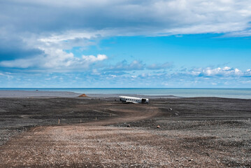 Scenic view of abandoned airplane wreck at black sand beach. Broken military aircraft in Solheimasandur on seashore. Famous tourist attraction on volcanic landscape against blue sky.