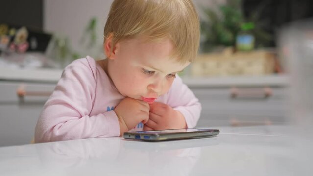 Cute Caucasian Baby Toddler Girl Watching Animated Movie Cartoon on Bright Screen Smartphone