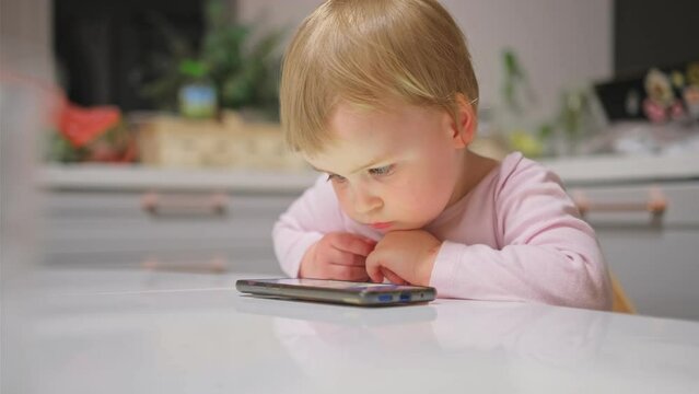 Cute Caucasian Baby Toddler Girl Watching Animated Movie Cartoon on Bright Screen Smartphone