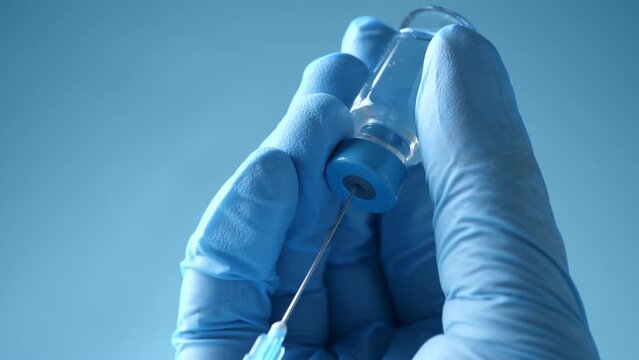 Doctor in blue latex gloves fill in syringe with medicine from glass vial, closeup. Making a vaccine injection