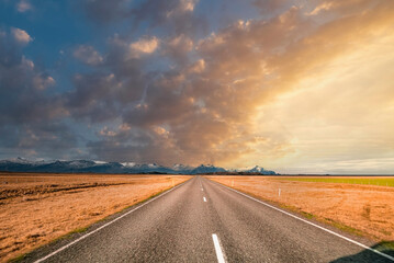View of empty diminishing street amidst volcanic landscape. Scenic view of mountain range against cloudy sky. Road markings on vanishing road in valley during sunset.