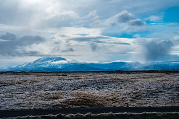 Scenic view of road by grassy landscape. Beautiful view of snow covered mountains against cloudy sky. Idyllic scenery of volcanic valley during winter.