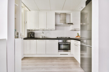Fragment of interior of light narrow home kitchen with minimalist style white furniture with sink...