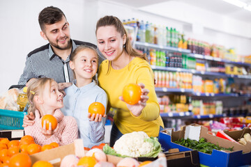 Glad parents with two daughters choosing sweet citrus fruits in food store