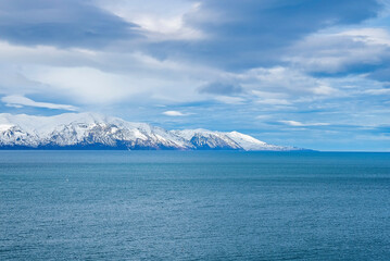 Scenic view of seascape and snowcapped mountains. Beautiful view of Atlantic ocean against cloudy sky. Idyllic scenery of sea and volcanic range during winter.