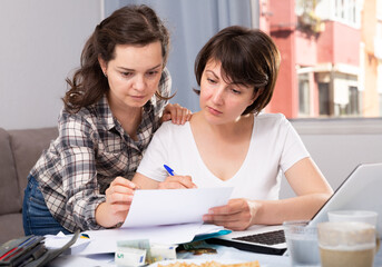 Obraz premium Portrait of serious women working with documents and using laptop at kitchen table