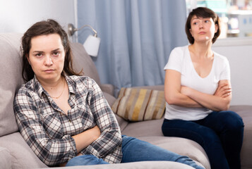 Sad young female and her elderly sister sitting at sofa during quarrel at home