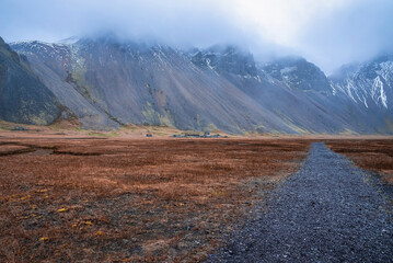 Pathway amidst field leading towards snowcapped mountains. Majestic ranges covered in fog....