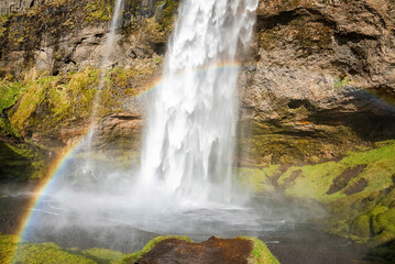 Fototapeta na wymiar Beautiful rainbow at Seljalandsfoss flowing from mountain. Scenic waterfall with mist in river. Idyllic view of famous attraction in valley of northern Alpine region.