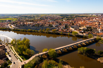 Fototapeta na wymiar Picturesque aerial view of Zamora city overlooking brownish tiled roofs of residential buildings and ancient arched bridge over Duero river on spring day, Spain