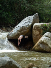 South American Man Jumping into the River from Large Rocks in the Middle of a Forest
