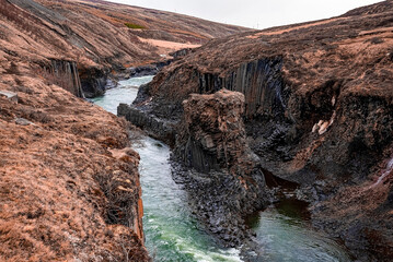 Stream flowing amidst basalt columns formation. Scenic view of rocky cliffs at Eastfjords against...