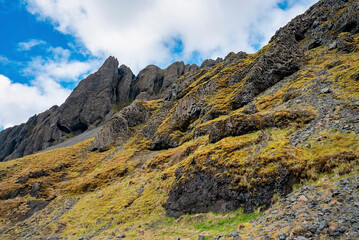 Scenic view of rock formations on mountain. Low angle view of patterned rocks on cliff against cloudy sky. Beautiful scenery of volcanic landscape in Alpine region.