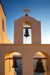 The bell tower of white church on Santorini island during orange sunset. - obrazy, fototapety, plakaty