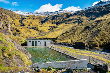 Beautiful geothermal Seljavallalaug against green mountain range. Scenic view of natural hotspring...