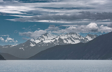 Skagway, Alaska, USA - July 20, 2011: Taiya Inlet above Chilkoot Inlet. Wide landscape with snow covered mountains along gray-blue ocean water under blue cloudscape.